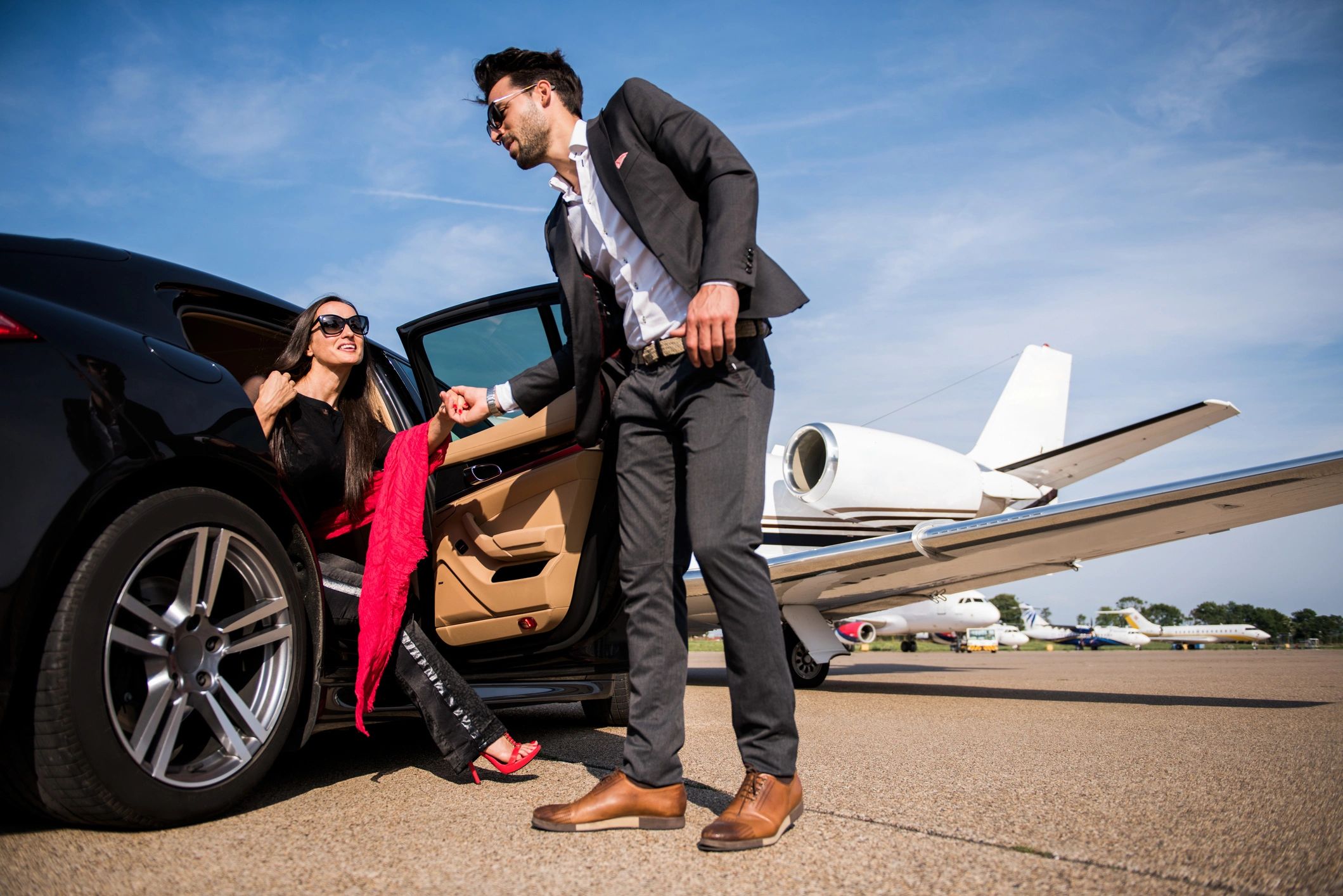 Stylish couple beside luxury vehicle at private jet tarmac